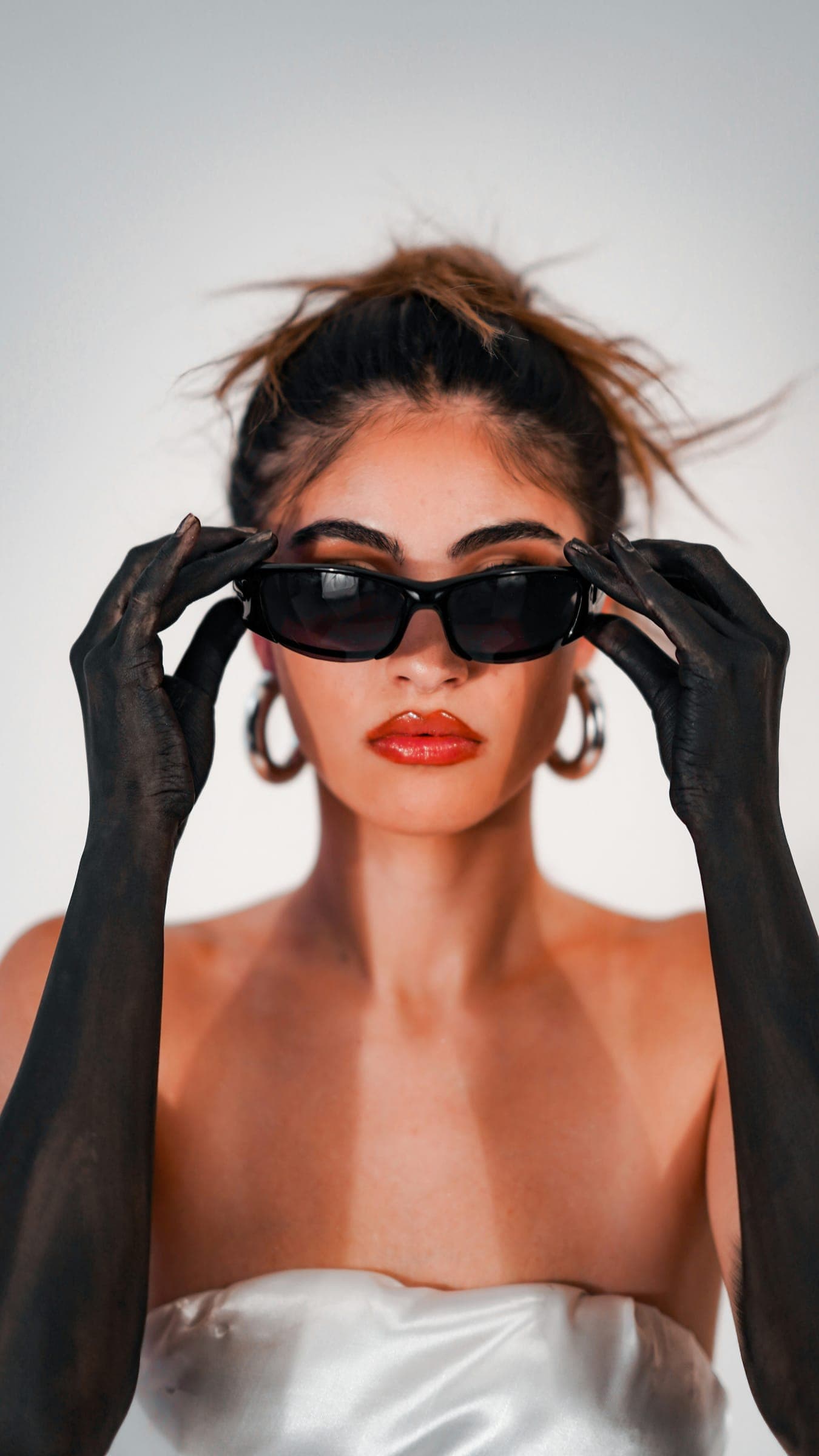 Close-up of a model with red lips adjusting black sunglasses with black-painted hands