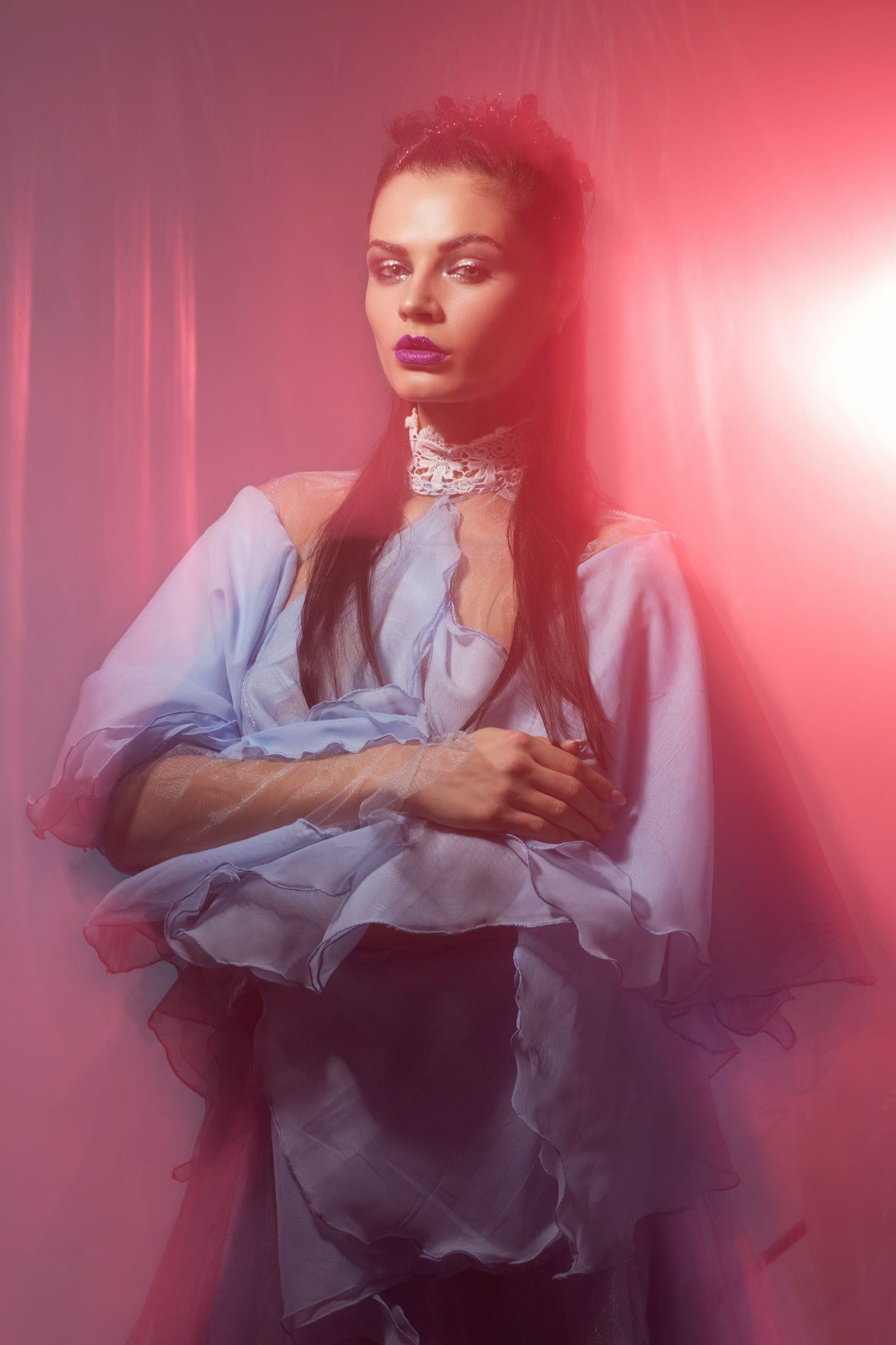 A model in a pale ruffled dress and plum lipstick, washed in soft pink light