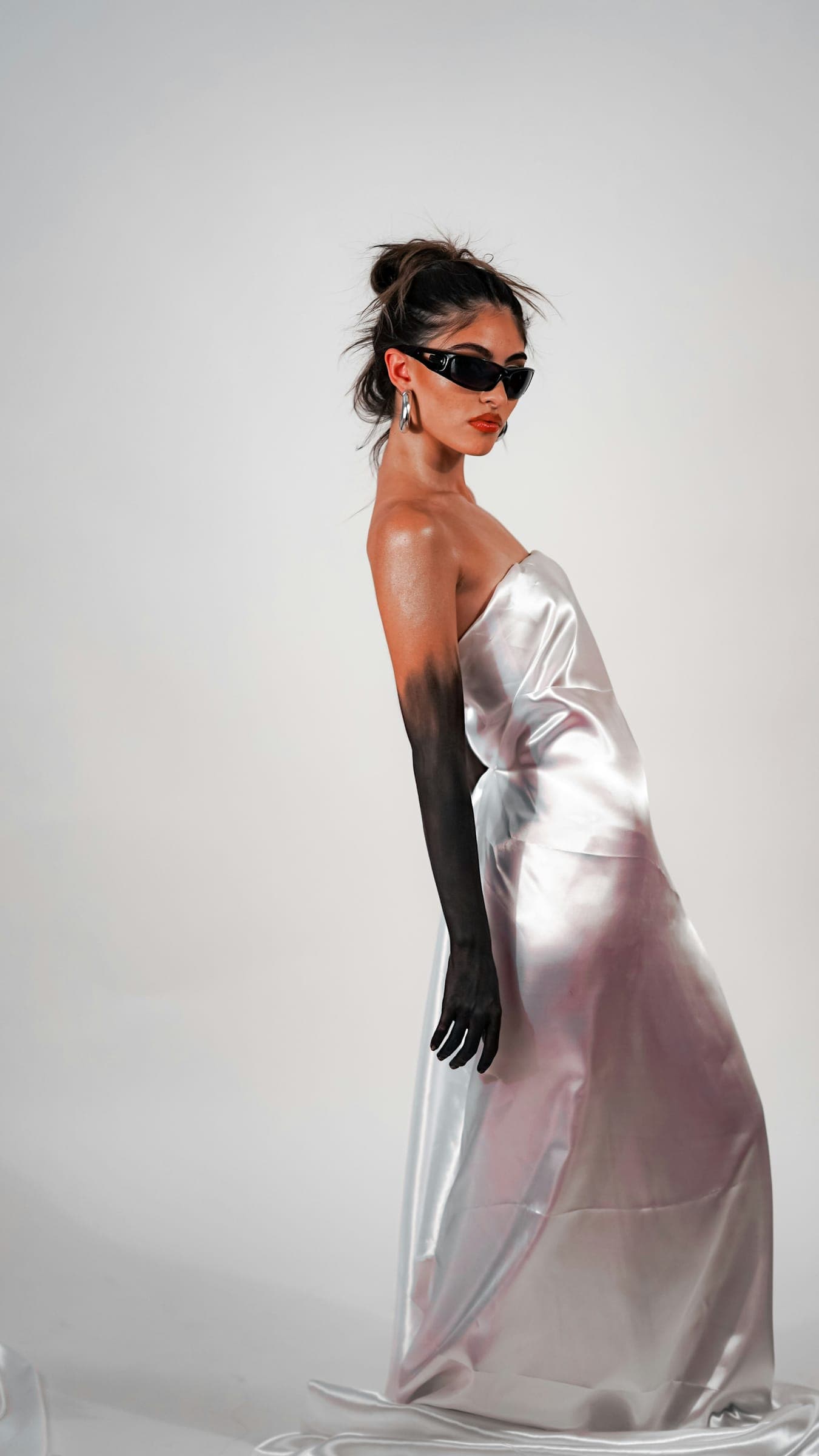 A model in a silver satin gown and black sunglasses, one arm painted black