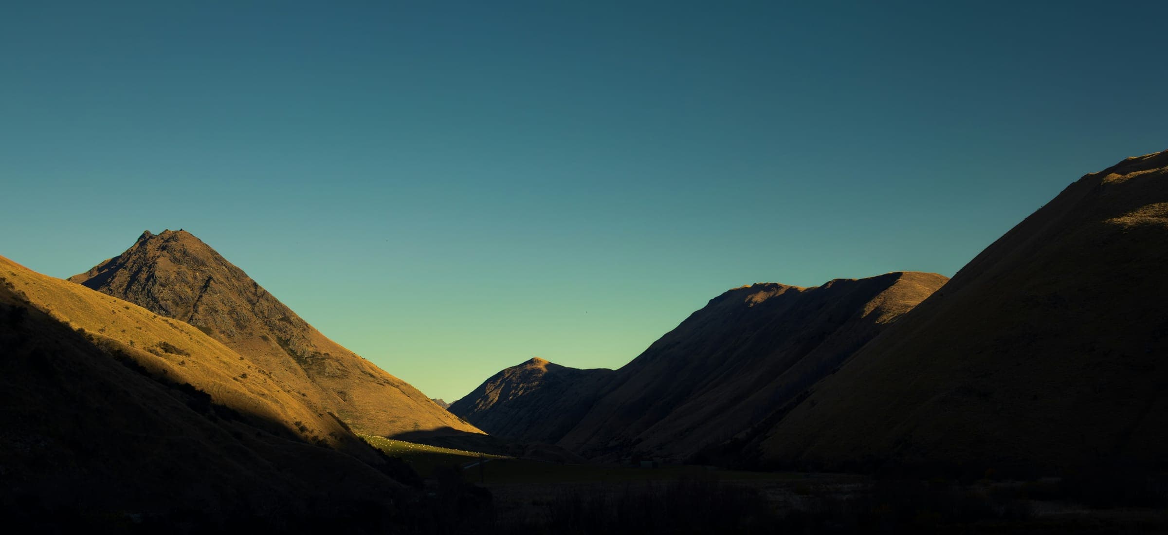 Mountain ridges against a teal dusk sky, the last light on one slope