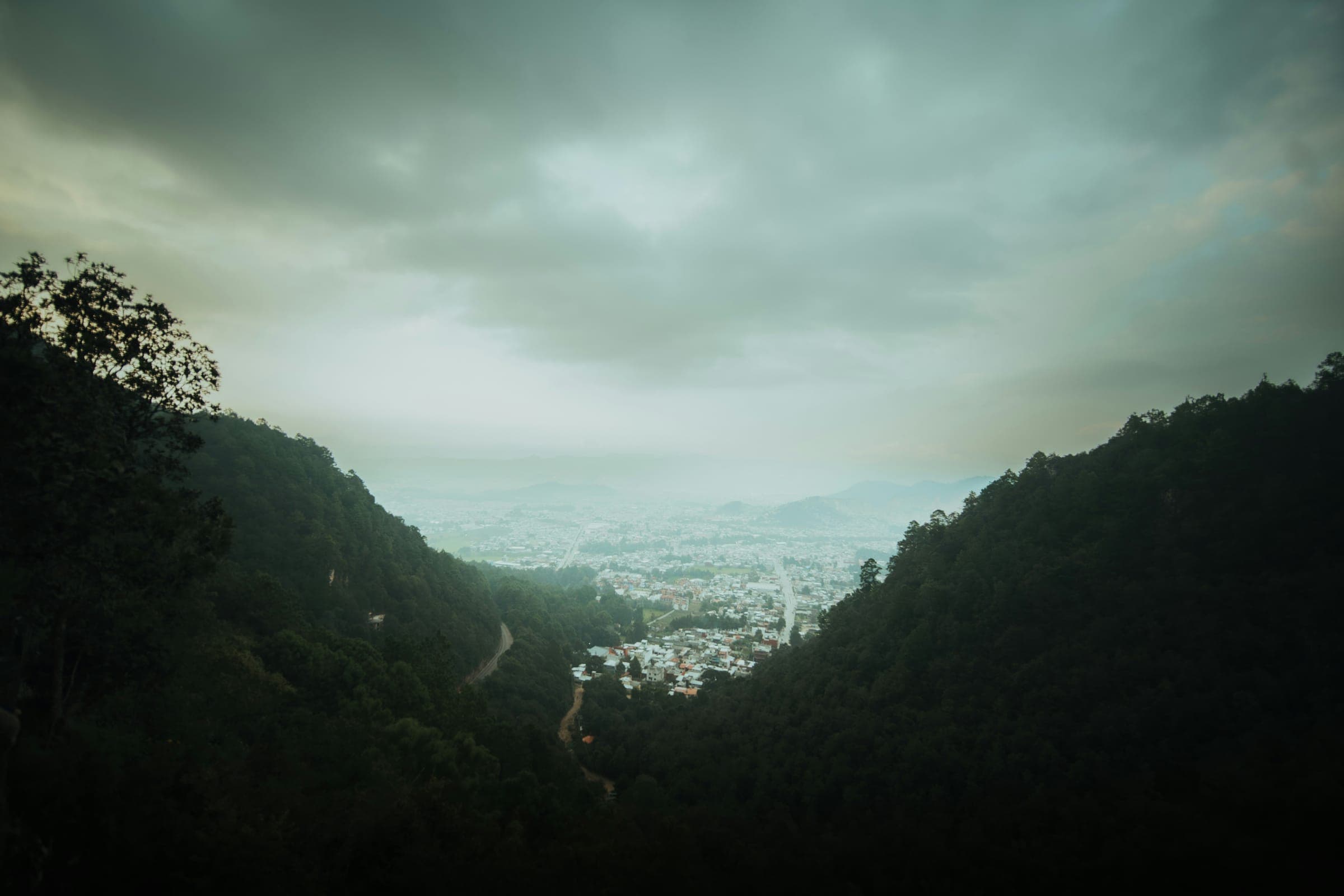 A misty green valley opening onto a town under a heavy sky