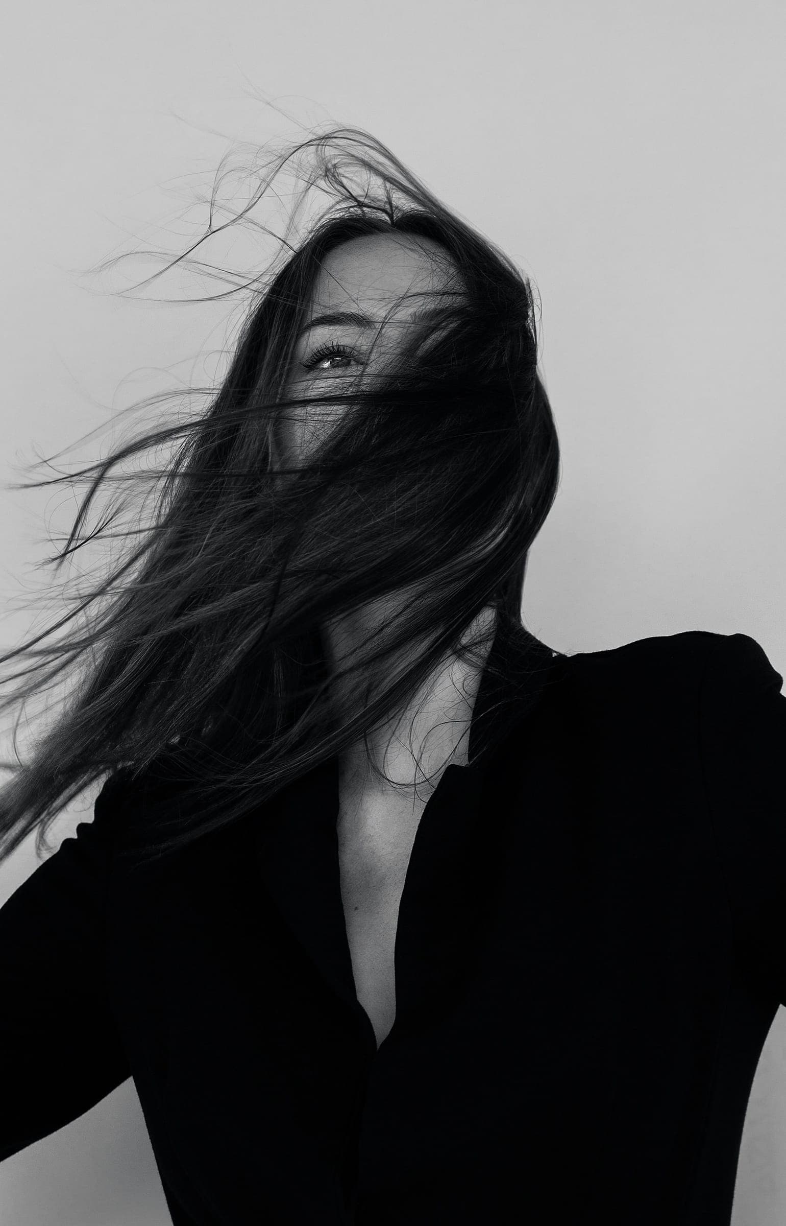 Black and white portrait in a dark shirt, long hair blowing across the face
