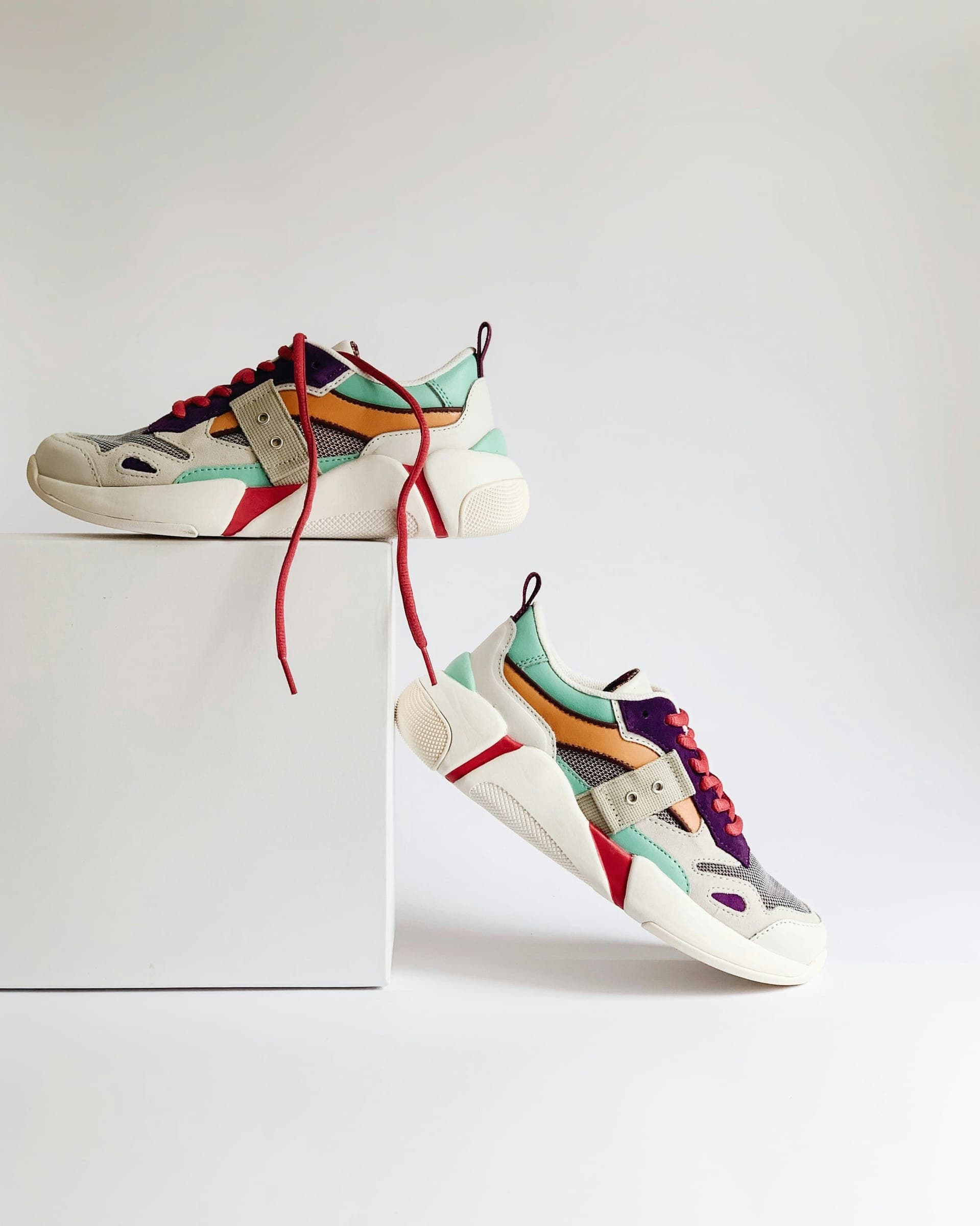 Two colourful sneakers on a white plinth, red laces trailing