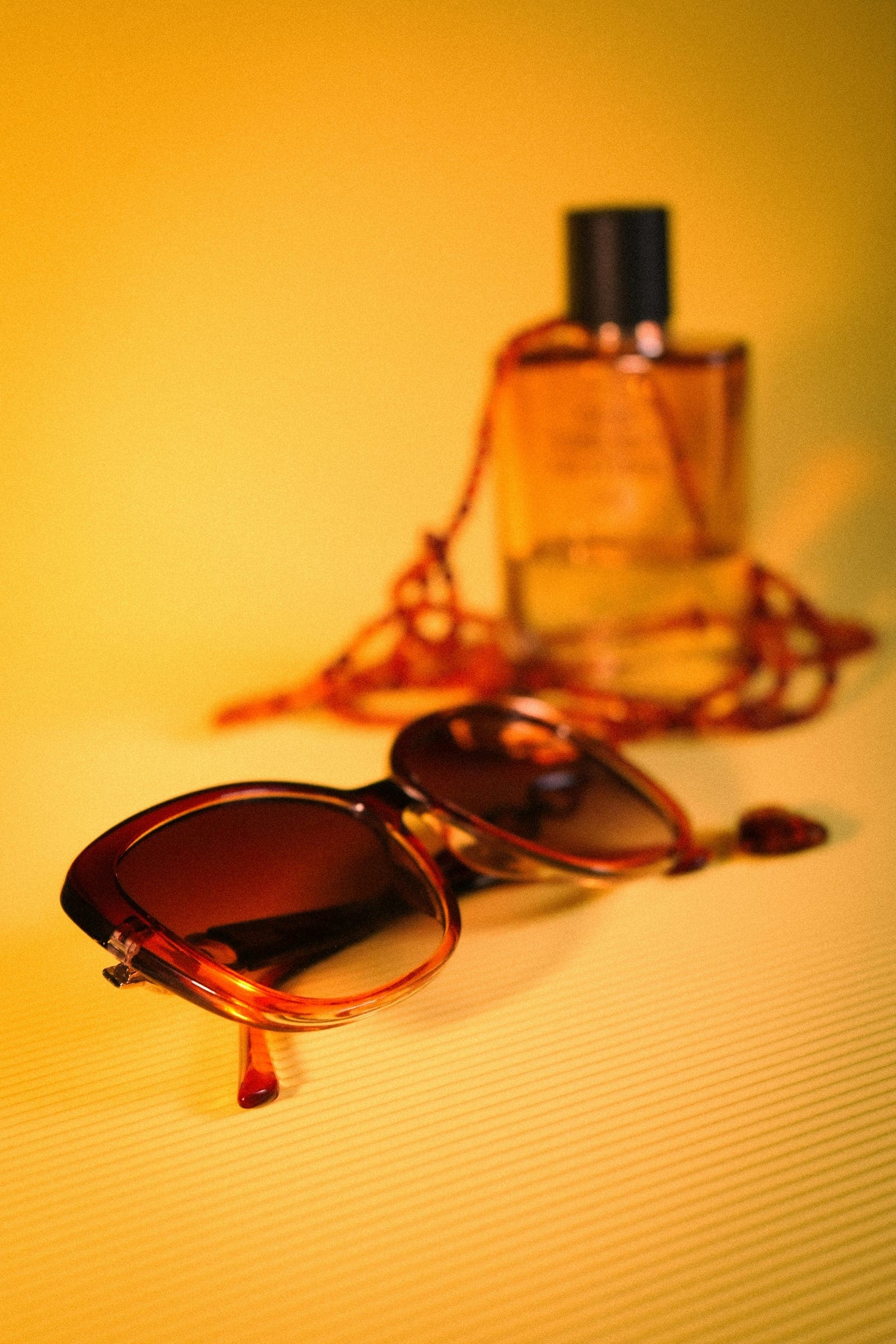 Tortoiseshell sunglasses and a perfume bottle on a warm yellow background