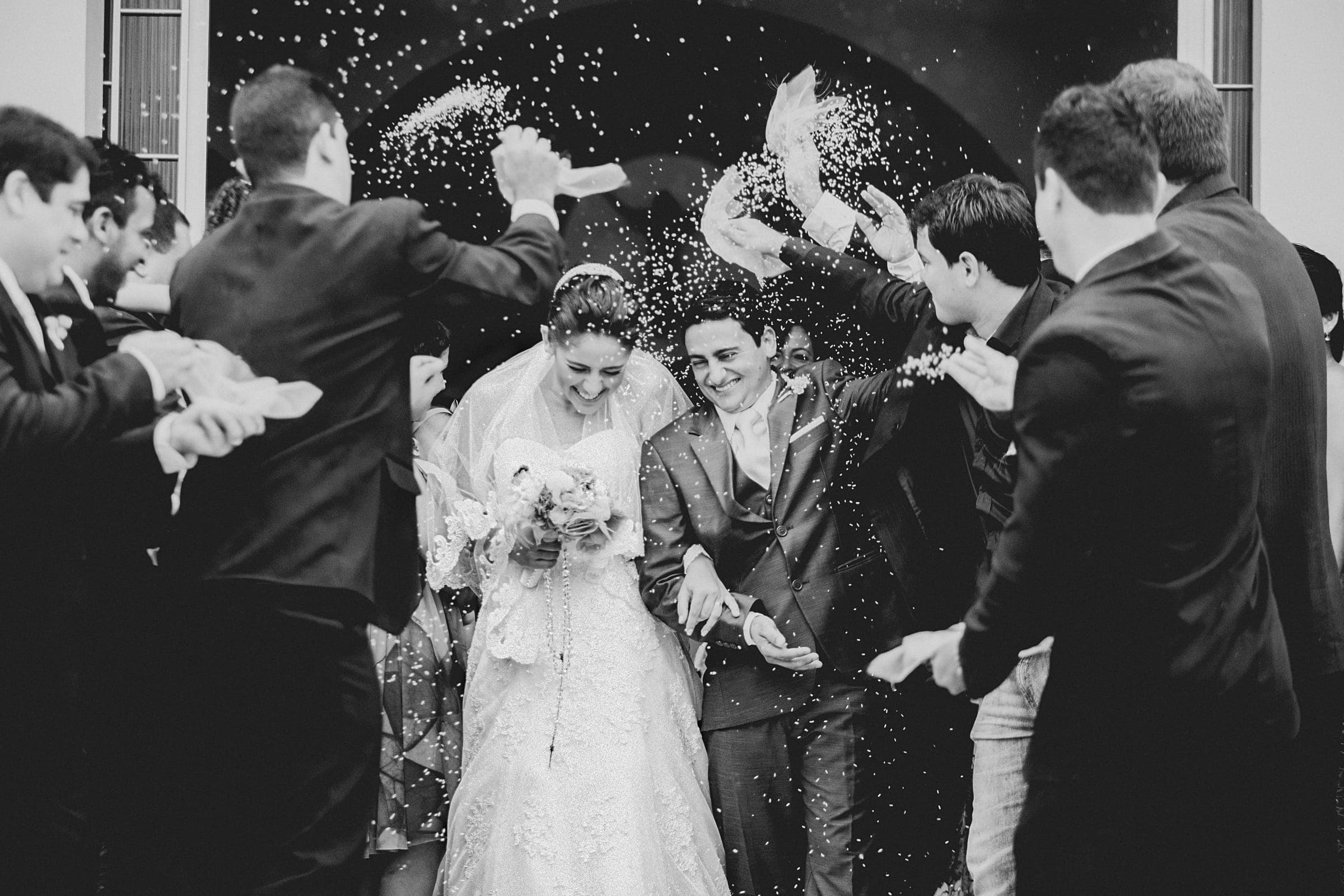 Black and white: a bride and groom laugh as guests throw rice over them