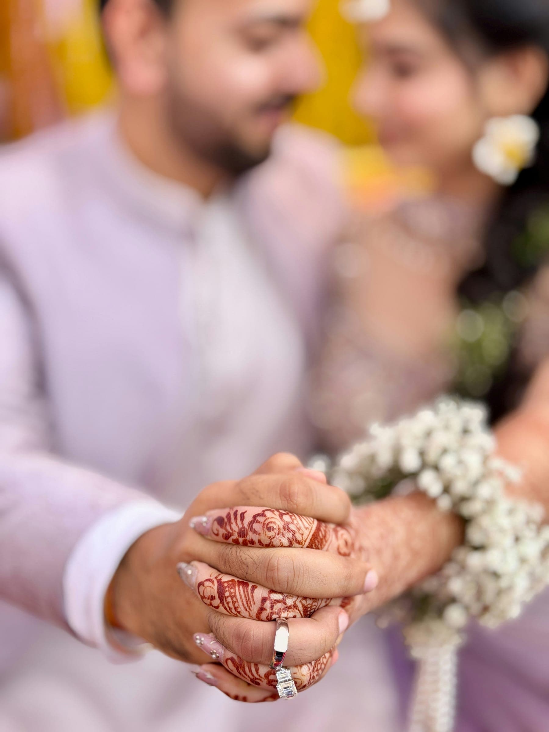 Close-up of a couple's joined hands, the bride's covered in mehendi, a ring on one finger